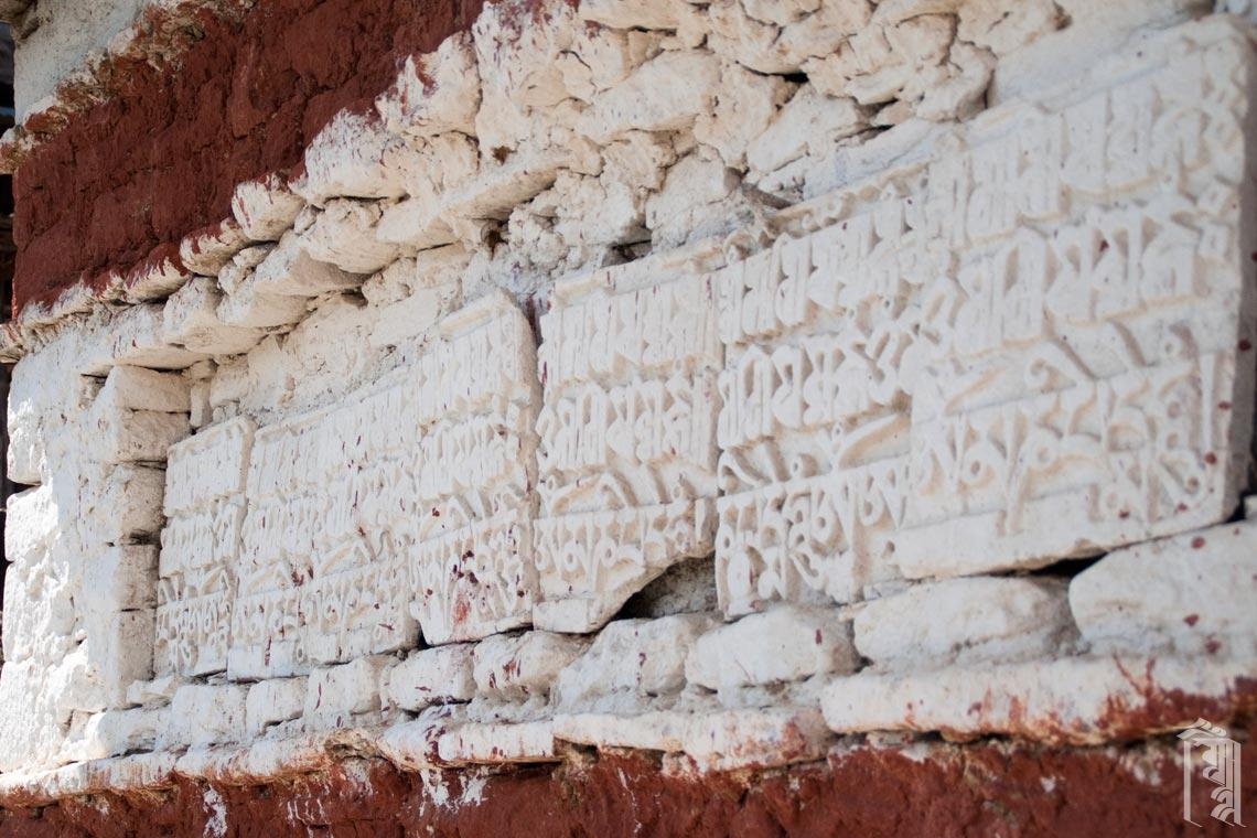 Eine weiß getünchte Gebetsmauer mit tibetischer Schrift, die tief in Stein gehauen ist und sich in der Mon-Region im Nordosten Indiens befindet.